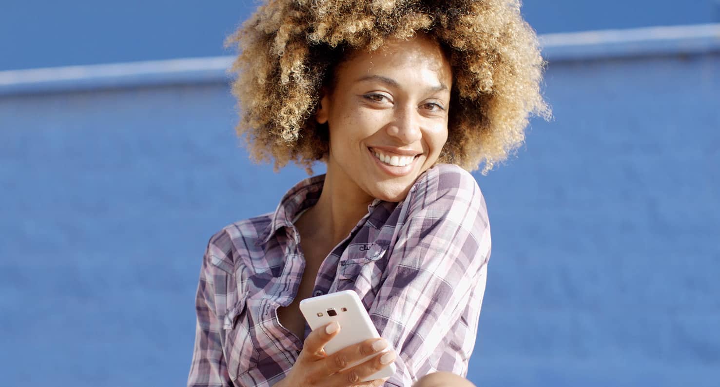 Happy woman in a flannel shirt smiling at camera and holding a iphone.
