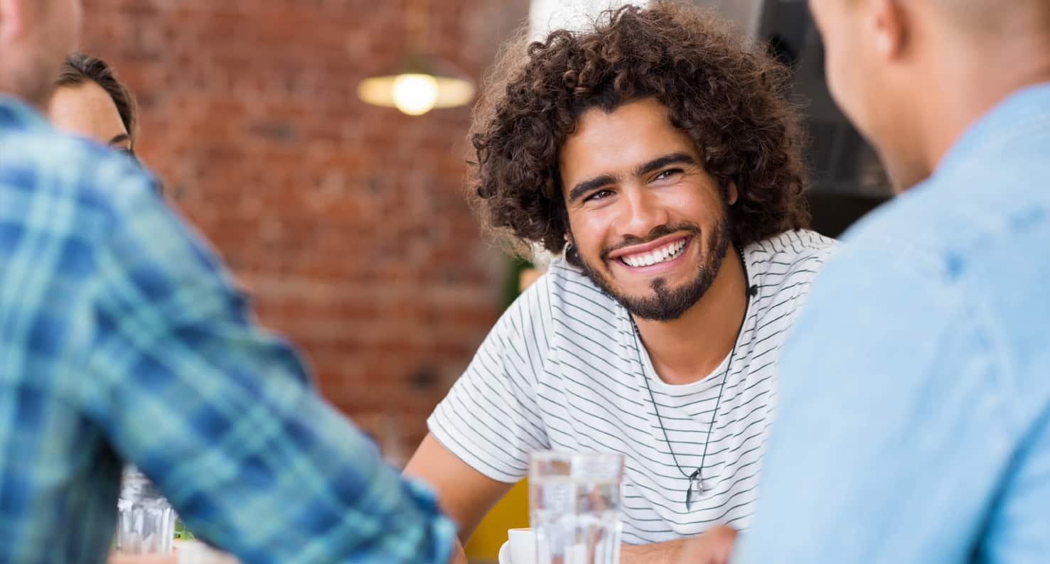 Smiling young man with curly hair, chatting with friends in a coffee house.