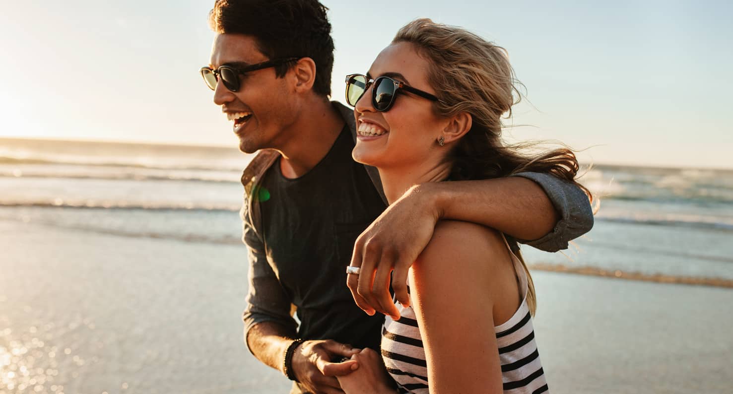 man and woman in sunglasses laughing on beach