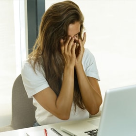 woman rubbing her eyes at her laptop