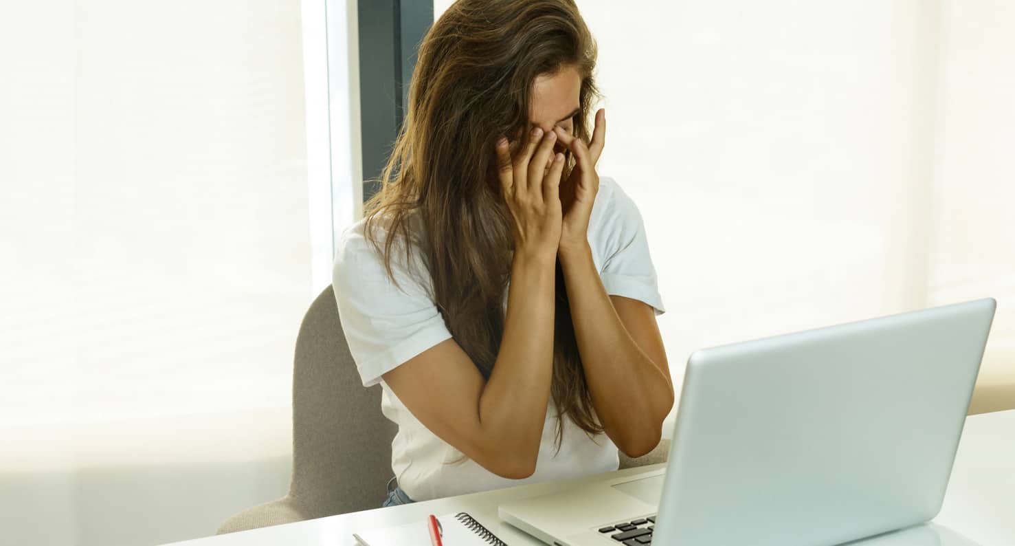 woman rubbing her eyes at her laptop