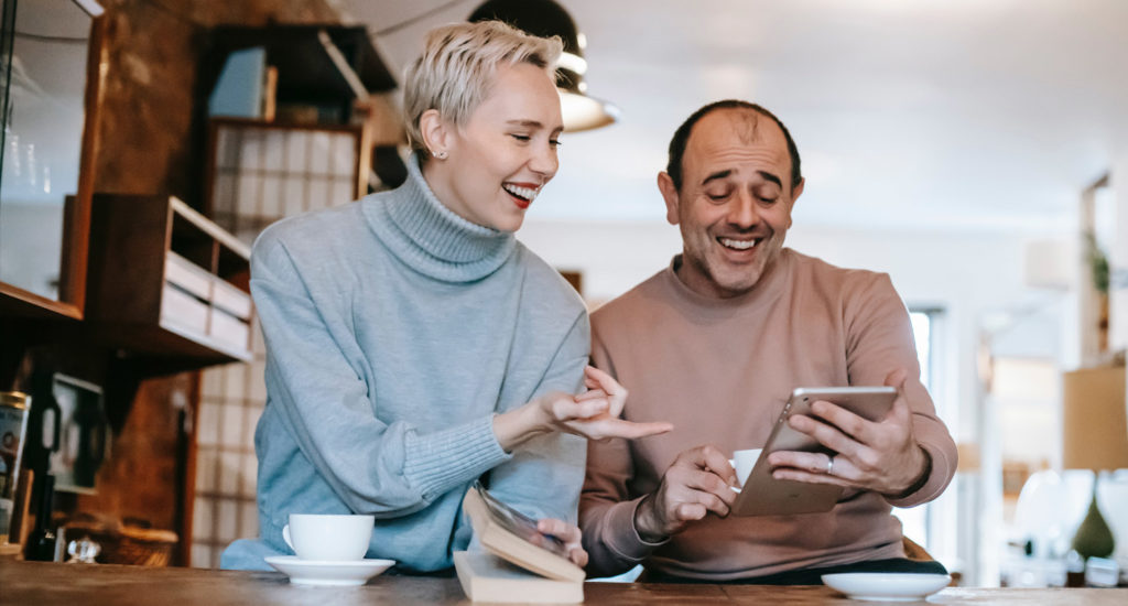 a middle aged couple enjoy books and tablets in the kitchen with no reading glasses